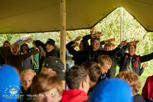 Jongeren dansen en juichen enthousiast onder een grote tent tijdens een groepsactiviteit bij de Young Solar Challenge.